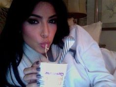 a woman is eating from a cup while holding a fork and spoon in her hand