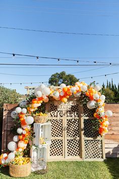 an orange and white wedding arch decorated with balloons, garlands and lanterns in front of a wooden gate