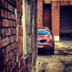 a red car parked in an alley between two brick buildings with garage doors on either side