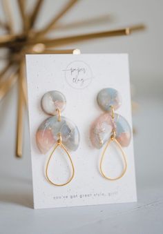 a pair of pink and blue earrings sitting on top of a white card next to a gold ear pin