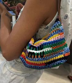 a woman holding a colorful crocheted purse on her left hand and cell phone in her other hand