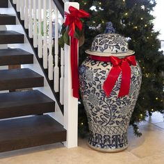 a large blue and white urn sitting next to a christmas tree with red ribbon