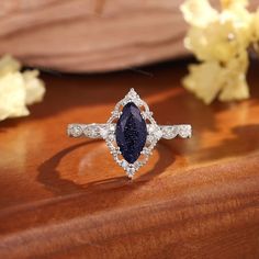 a diamond and blue stone ring sitting on top of a wooden table next to flowers