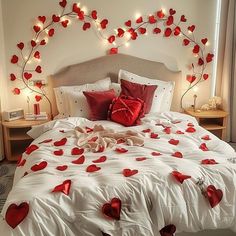 a bed with white sheets and red hearts on the comforter is decorated with lights