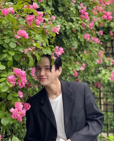 a man standing next to a bush with pink flowers growing on it's sides