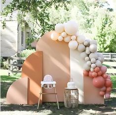 an outdoor party setup with balloons and decorations on the wall, including a baby's highchair