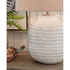 a white vase sitting on top of a wooden table next to a lampshade