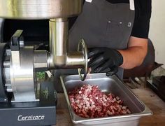 a man in black shirt and gloves preparing food inside of a metal container on top of a table