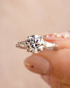 a woman's hand holding an engagement ring with a diamond in the center and side stones on it