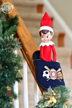 an elf is sitting on top of a christmas tree with a blue bag in front of him