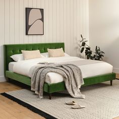 a bed with green headboard and foot board in a white room next to a potted plant