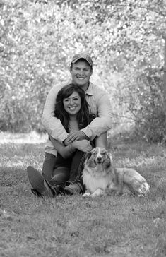 a man and woman sitting in the grass with their dog