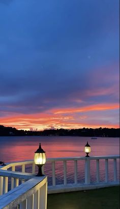 two lamps are lit up on the balcony overlooking the water at sunset or dawn with clouds in the sky