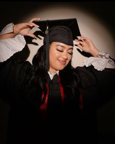 a woman wearing a graduation cap and gown holding her hands up to her head with one hand