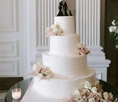 a white wedding cake with pink flowers and two figurines on top