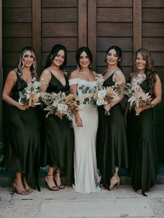 a group of women standing next to each other in front of a wooden door holding bouquets