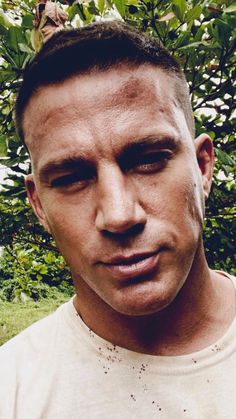 a close up of a person wearing a white t - shirt with trees in the background