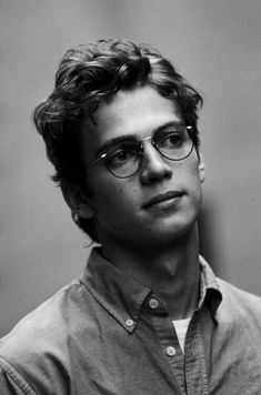 a black and white photo of a man with glasses looking off to the side in front of a wall