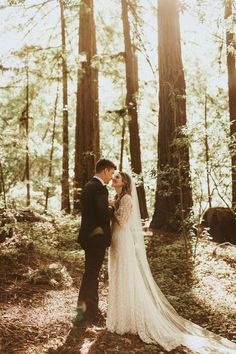 a bride and groom standing in the woods