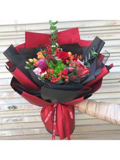 a bouquet of flowers wrapped in black paper and tied with a red ribbon is being held by a person