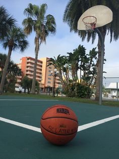 an orange basketball sitting on top of a green court next to palm trees and buildings