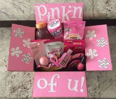 a pink box filled with lots of items on top of a marble counter next to a sign