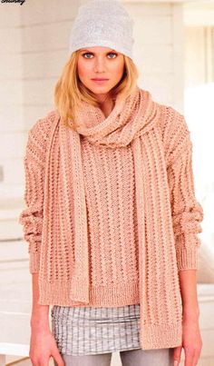 a woman wearing a hat and scarf standing in front of a white wall with her hands in her pockets