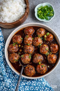 meatballs with sauce and green onions in a bowl next to rice on a table