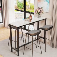 a dining table with two stools and a vase filled with flowers on the side