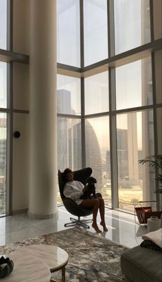 a man is sitting in a chair looking out the window at the cityscape