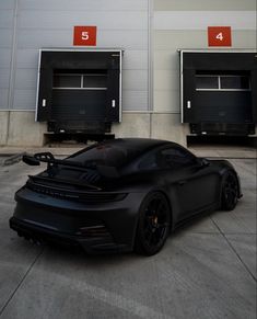 a black sports car is parked in front of three garage doors with red numbers on them