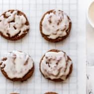 six cookies with icing on a cooling rack next to a cup of coffee and spoon