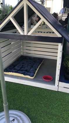 a dog house made out of pallets with a bed in the middle and a red bowl on the ground