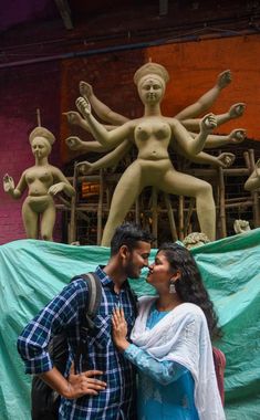 a man and woman standing next to each other in front of a statue with arms around each other