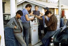 four men are filling up their cars at a gas station