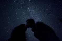 two people are kissing under the stars in the night sky, with one person holding his head