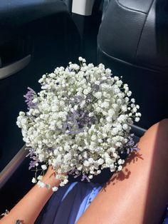 a bouquet of white flowers sitting in the back seat of a car on someone's lap