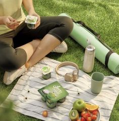 a woman is sitting on the grass with her food and drink in front of her