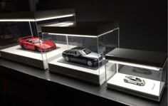 three models of cars are displayed in glass cases on a black surface with white lighting