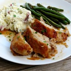 a white plate topped with meat, mashed potatoes and green beans on top of a wooden table