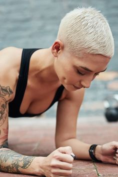 a woman with white hair and tattoos is laying on the ground looking at her cell phone