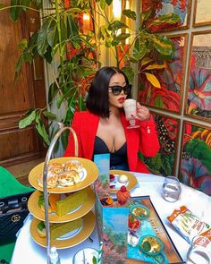 a woman sitting at a table with plates and cups in front of her, holding a drink