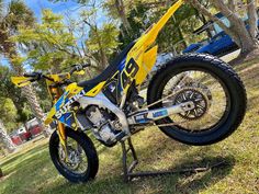 a yellow and blue dirt bike parked on top of a grass covered field next to trees