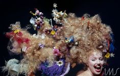 a woman with curly hair and flowers on her head posing for a photo in front of a black background