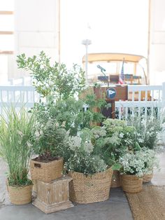 some plants are sitting in baskets on the ground next to a table with chairs behind them