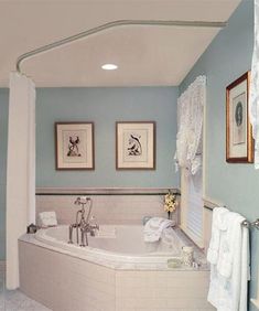 a bath tub sitting next to two pictures on the wall in front of a window