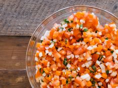 a glass bowl filled with chopped vegetables on top of a wooden table