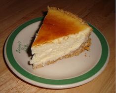 a piece of cheesecake on a green and white plate sitting on a wooden table