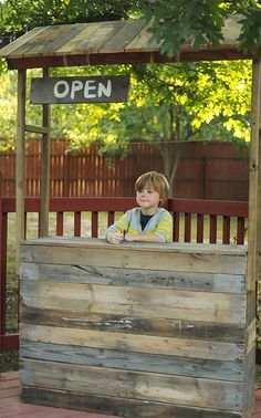 a young boy sitting on top of a wooden bench next to a sign that says open