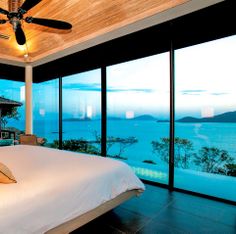 a bedroom with large windows and a ceiling fan in the room that overlooks the ocean